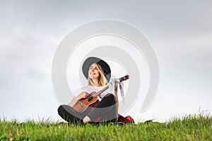 Outdoor portrait of a young beautiful woman in black hat, playing guitar. Space for text