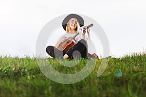 Outdoor portrait of a young beautiful woman in black hat, playing guitar. Space for text