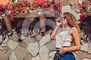 Outdoor portrait of young beautiful woman with long curly hair wearing summer casual outfit in city by flowers. Fashion model