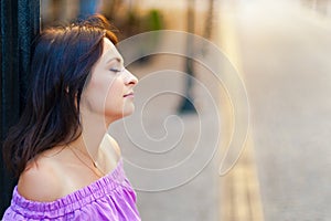 Outdoor portrait. Young beautiful woman lost in thought while visiting the city center on a sunny day, in a purple dress with the