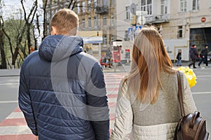 Outdoor portrait of young couple walking on city street, happy young man and woman on zebra crossing, back view, urban background