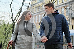 Outdoor portrait of young couple walking with suitcase on city street, happy young man and woman travel in spring,urban background