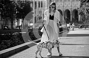 Outdoor portrait of young elegant woman walking in street. Young fashion model walking with dog, urban style.