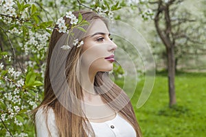 Outdoor portrait of young woman with natural makeup and healthy long brown hair in blossom park outdoors. Natural female beauty