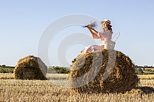 Outdoor portrait of young woman in a pink dress sitting on hay bale