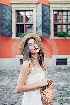 Outdoor portrait of young woman wearing stylish dress and accessories in old Lviv city. Fashionable straw hat and purse