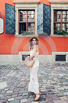 Outdoor portrait of young woman wearing stylish dress and accessories in old Lviv city. Fashionable straw hat and purse