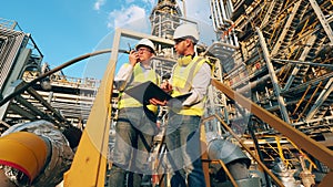 Outdoor premises of the oil refinery with two engineers talking