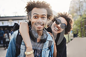 Outdoor protrait of african-american couple hugging and smiling broadly at camera while walking in park and expressing
