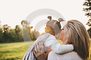 Outdoor rear view of cute girl kid playing with her mother outside. Portrait of woman telling secret to her child spending time in