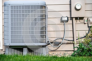 Outdoor residential air conditioner on an elevated pad. Electrical utility hookups on building exterior.