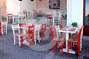 Outdoor restaurant with white table and red chairs, Crete, Greece.