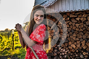 Outdoor right sunnny portrait of happy teen red head girl in red dress that standing with rakes and looking at the