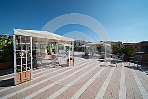 Outdoor rooftop terrace with sunshade, and chairs and desks in a sunny day