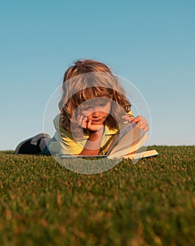 Outdoor school, motivation learning kids. Child boy is reading a book on the spring park. Relaxing on the grass in the