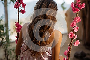 Outdoor serenity Woman on swing, hair graced by flowers, captured from behind photo