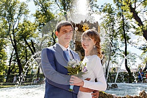 Outdoor shot of bride and groom standing near fountain in park