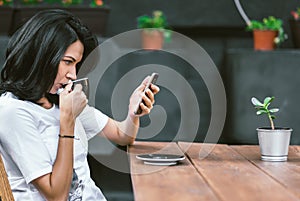 Outdoor shot of Caucasian girl in white t-shirt enjoying free wi-fi at coffee shop, surfing internet on mobile phone, reading