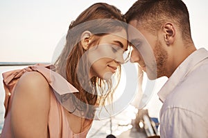 Outdoor shot of cute couple in love, closing eyes and touching with foreheads while sailing on yacht, having vacation