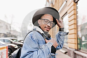 Outdoor shot of fashionable brunette guy with light-brown skin. Photo of carefree african man in denim attire chilling