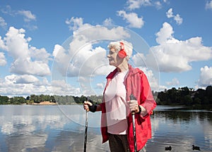 Outdoor shot of healthy energetic elderly female walking on the beach sunny day using Nordic poles.