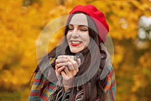 Outdoor shot of pretty girl with morning coffee in thermos cup, charming woman expressing happyness, female wrapped warm checkered