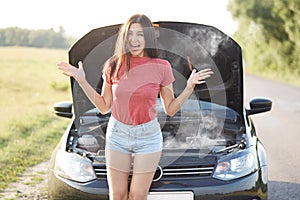 Outdoor shot of puzzled young female driver gestures angrily, be