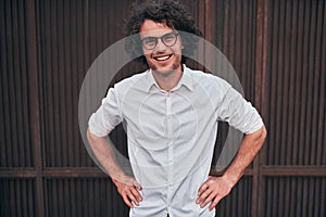 Outdoor shot of smilimg handsome young businessman with glasses posing outdoors. Male student posing against brown wall. Smart guy