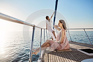 Outdoor shot of tender and attractive adult female, spending time on boat. Girl stands on bow of yacht with dreamy look
