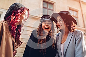 Outdoor shot of three stylish young women talking on city street. Friends laughing and having fun