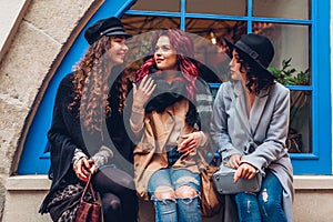 Outdoor shot of three young women chatting and laughing on city street. Best friends talking and having fun by cafe