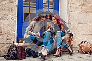 Outdoor shot of three young women looking at smartphone and laughing on city street. Girls talking and having fun