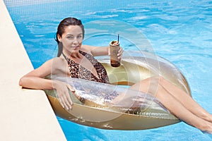 Outdoor shot of young brunette woman with wet hair relaxing on inflatable swim ring, wearing fashion swimwear with leopard print,
