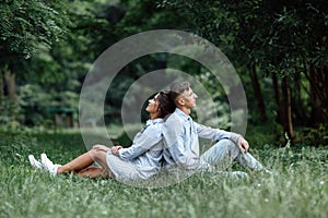 Outdoor shot of young happy couple in love sitting on grass on nature. Man and woman hugging, sunlight in summer park. Happy