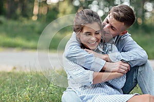 Outdoor shot of young happy couple in love sitting on grass on nature. Man and woman hugging  sunlight in summer park. Happy
