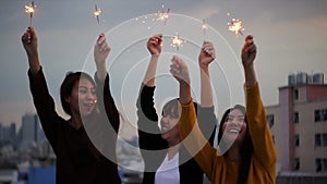 Outdoor shot of young people at rooftop party. Happy group of asia girl friends enjoy and play sparkler at roof top party.