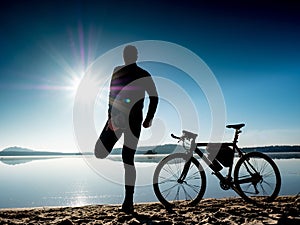 Outdoor silhouette of fit cyclist in cap at sunset with reflection in water