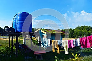 Outdoor simple blue plastic cistern and hut and clothes drying photo