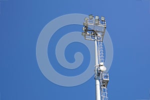 Outdoor stadium lights and telecommunication tower against daytime blue sky.