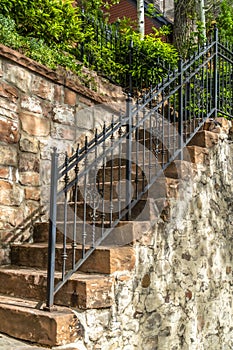 Outdoor staircase with stone steps and black metal railing against a fence