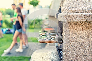 Outdoor stone stove with grill and skewers. Company of friends at barbecue party at park or backyard with green grass lawn and
