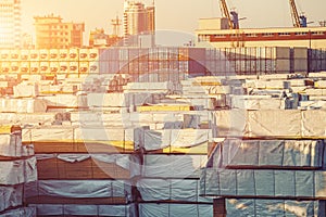 Outdoor storage in freight port with pallets, stacks and containers of building material goods for construction at sunset