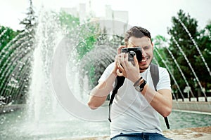 Closeup portrait of handsome young man taking photo in city park. Stylish boy in a white tshirt, with bagpack taking photos