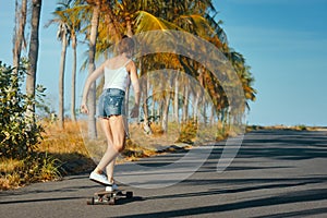 Outdoor summer portrait of cheerful young woman riding longboard in sunny day.