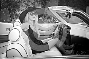 Outdoor summer portrait of stylish blonde vintage woman driving a convertible retro car. Fashionable attractive fair hair female