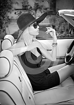 Outdoor summer portrait of stylish blonde vintage woman driving a convertible retro car. Fashionable attractive fair hair female