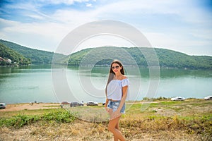 Outdoor summer portrait of young pretty long-haired brunette woman enjoying nature on mountain lake. Summer traveling, holiday.