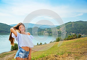 Outdoor summer portrait of young pretty long-haired brunette woman enjoying nature on mountain lake. Summer traveling, holiday.