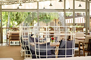 Outdoor summer restaurant terrace, with white metal and wooden furniture, sofa cushions, flowers, canopy, sun protection