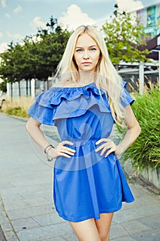 Outdoor summer smiling lifestyle portrait of pretty young woman. Long blond hairs, blue outfit in park. Blue dress.